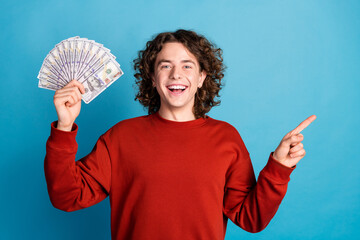 Photo of funky cool guy dressed red pullover rising cash fan pointing emtpy space isolated blue...