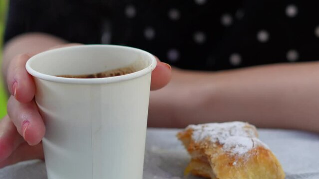 close up of woman eating bakery and drinking coffee from paper cup.