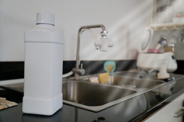 White plastic bottle of dish soap sits on the edge of a stainless steel sink.
