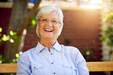 Portrait, laugh and senior woman on bench for retirement, relax and glasses in garden. Joke, seat...