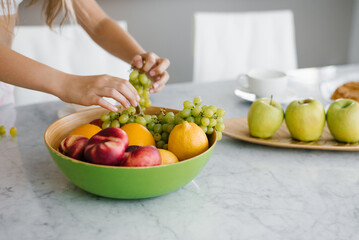 Close up of children's hands of a girl taking fresh grapes from a plate on the table in the kitchen