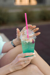 Refreshing non-alcoholic cocktail in a plastic cup with a straw in the hands of a woman