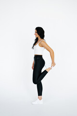Young female fitness trainer wearing sportswear on white background full-length, stretching the front surface of the thighs
