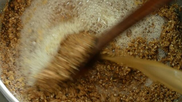 Man's hand stirs malt with a large spoon during the mashing process to produce beer wort