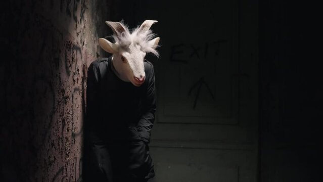 Scary man in a mask shaking on a ruined wall.