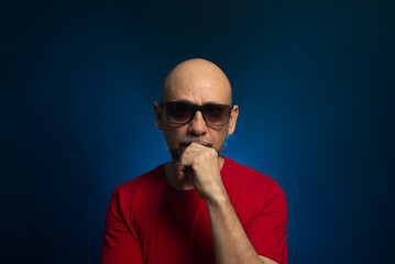 Obraz premium Bald bearded man wearing red shirt with hand on chin looking at camera. portrait in studio.