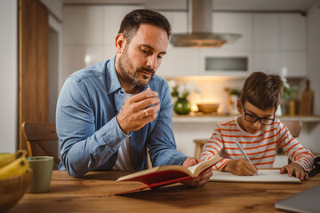 Father with book assistance and help son to do homework together home