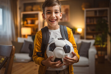Portrait of young boy with back pack stand and hold football ball