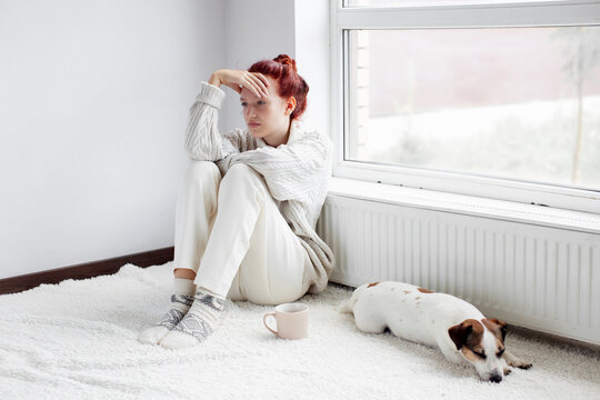 Sad young Woman sitting near radiator at home