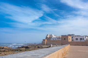 Tourists relax on the ancient seaside walls of Essaouira under a clear blue sky with soaring...