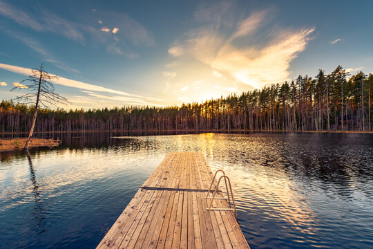 Small forest lake. Sunset behind the forest. Wooden bridge. Small waves. View from the bridge. Summer day. View from the shore. Beautiful nature. Russia, Europe.