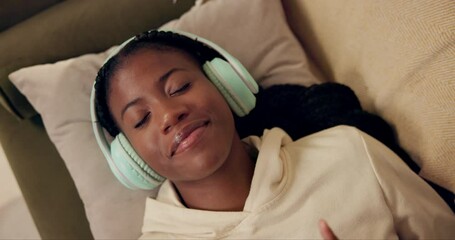African woman, headphones and above on couch with smile, relax and peace with music in home living room. Girl, listening and happy for streaming, audio subscription and lying on lounge sofa in house
