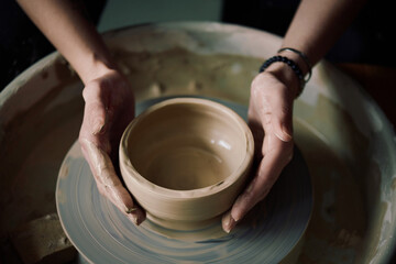 From above view of hands of unrecognizable female artisan shaping bowl on potters wheel