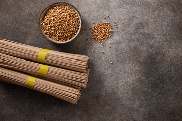 Uncooked buckwheat noodles, soba and grain in bowl on dark gray background. View from above. Space for text. Healthy vegan diet. Alternative gluten free pasta.