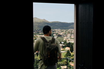 Travel and adventure concept. A young man with a retro-style green backpack stays in old town Bar...