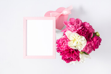 Holiday floral background with peonies. Pink peonies, photo frame for text and heart-shaped gift on white background. Birthday, Wedding, Mother's Day, Valentine's day, Women's Day. Flat lay