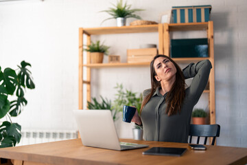 Young woman sitting on chair at home and feeling tired after working on her laptop.