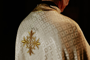 Rear view medium closeup of unrecognizable Catholic priest wearing dalmatic standing in church