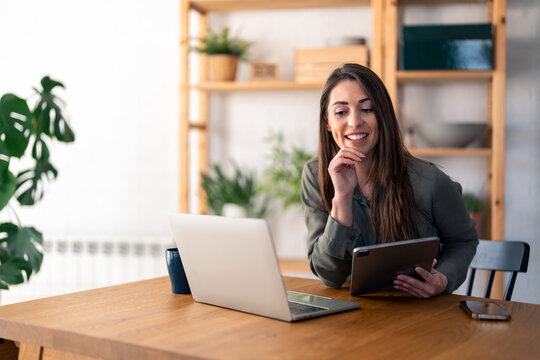 Happy female business professional discussing over video call on laptop while sitting at desk in home office.