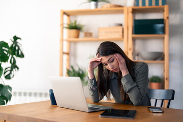 Sad overwhelmed businesswoman looking hopeless while working on laptop in home office.