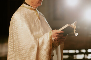 Crop shot of unrecognizable senior Catholic priest wearing liturgical vestment reading Bible, copy...