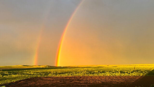 Double rainbow after a storm passed through with a dark background and golden sunshine hue with a highway in the background and fresh tilled dirt in the foreground in South Dakota