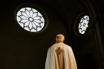 Rear view low angle shot of unrecognizable elderly Catholic priest wearing chasuble standing in...