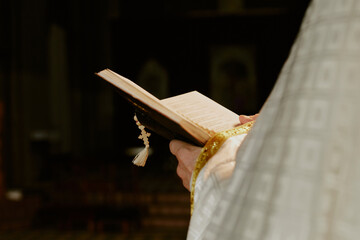 Closeup of hands of unrecognizable pastor holding prayer or Bible book with rosary on it