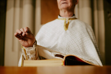 Selective focus shot of senior Catholic pastor wearing vestment praying while standing at lectern with book on it