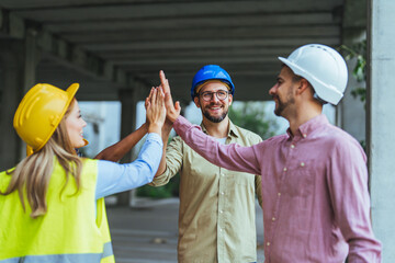 Diverse construction workers in safety helmets celebrate progress with a high five at a project...