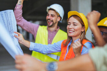 A diverse group of joyous male and female construction workers with hard hats and safety vests...