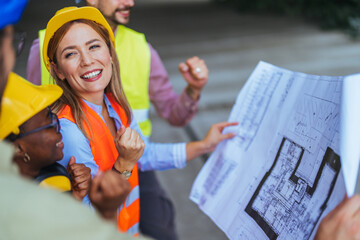 A group of diverse workers in safety gear shares a light moment while examining a construction...