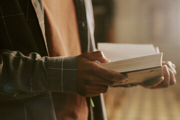 Closeup of hands of unrecognizable African American man standing indoors reading book