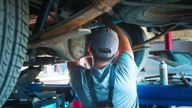 A mechanic in a blue uniform is focused on repairing the suspension system of a lifted vehicle, showcasing professionalism and expertise in the auto service field.