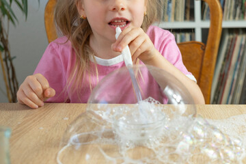 Little girl blows bubbles through plastic straw made of soap foam, kids fun games, diy soap...