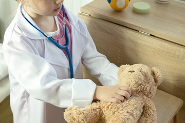 little child, blonde girl 4 years old plays with toy, little doctor carefully checking teddy bear's...
