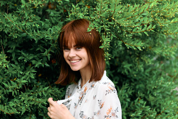 Vibrant woman with red hair standing against lush green foliage in the garden