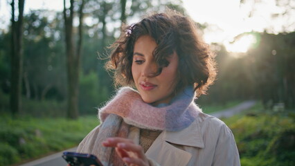 Casual woman browsing mobile phone in sunny park closeup. Portrait brunette