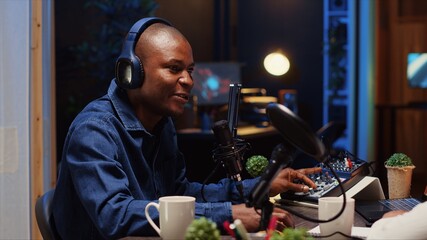 African american man recording podcast, adjusting microphone to ensure optimum sound quality for...