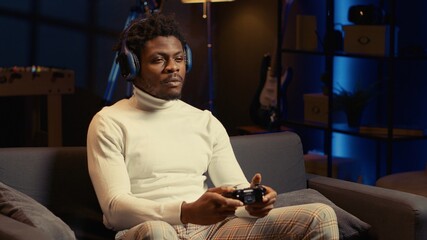 African american man playing videogames on console late at night, struggling to stay awake. Gamer...
