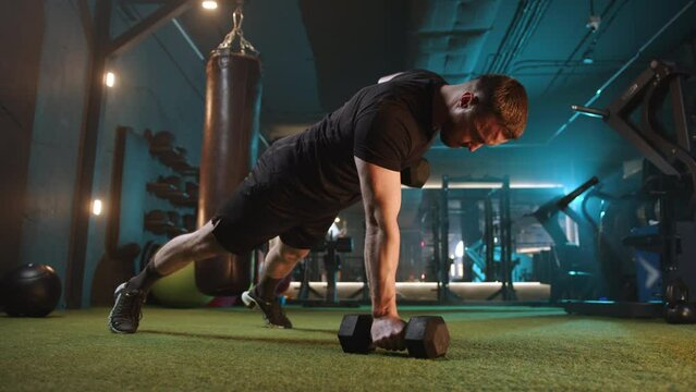 In a wellequipped gym, a man focuses on upper body strength and core stability by performing renegade rows with dumbbells. This workout emphasizes dedication, hard work, and achieving fitness goals