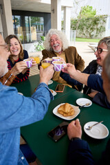 Vertical. Group of older friends gathered on terrace cafe toasting smiling with coffee. Caucasian seniors celebrating cheers together in cappuccino restaurant. Lifestyle happy people in nursing home