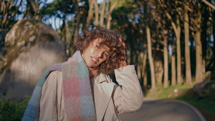 Fototapeta premium Playful woman posing sunlight park in scarf catching warm morning wind closeup