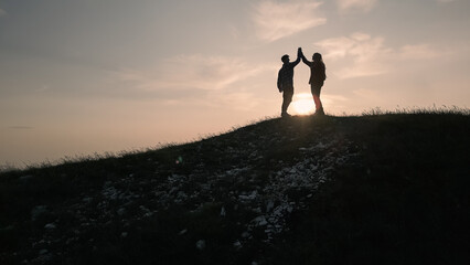Teenage hiking adventure, a cheerful teen girl and a teen boy giving high five on the mountain top, enjoying success. Fun, inspiration, and recreation concepts.