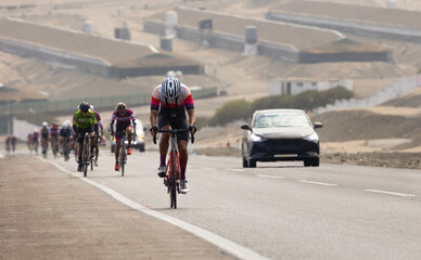 A large group of amateur cyclists in racing gear faces a challenging uphill on a traffic-heavy...
