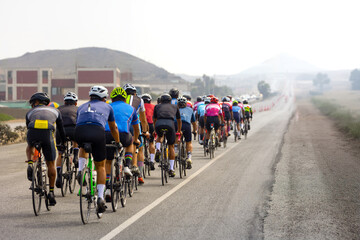 A large group of cyclists in uniform ride along a busy highway, navigating through fast-moving traffic, under cool and fresh weather conditions