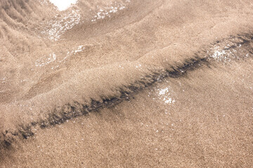 Close-up of beach sand stained with oil residue from an oil spill, showing the environmental impact on the shoreline