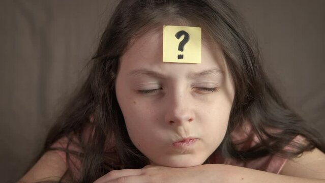 Child think about question decisions indoor. A little girl with pensive grimace try to think about task on her forehead.