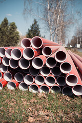 Stacked Red Plastic Pipes Beside Roadway On Sunny Day