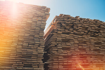 A large stack of lumber boards is neatly stacked at a lumber yard. The boards are arranged in a...